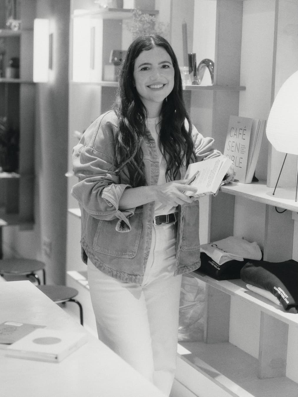 Guada sonriendo con un libro en la mano, junto a una estantería