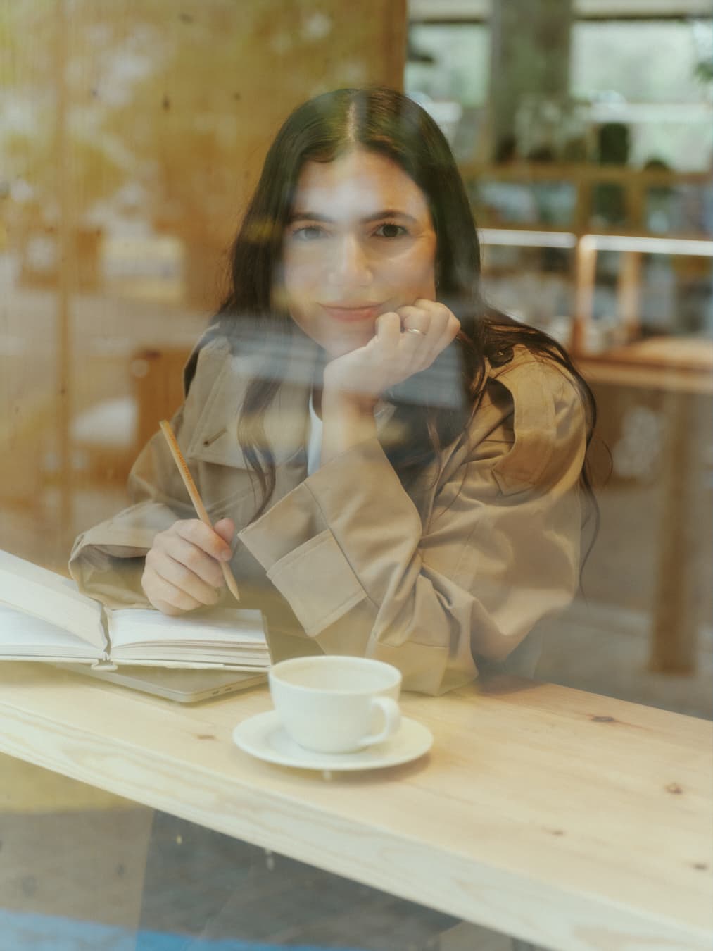 Guada detrás de un vidrio, con un café y un cuaderno, apoyando la cara en la mano